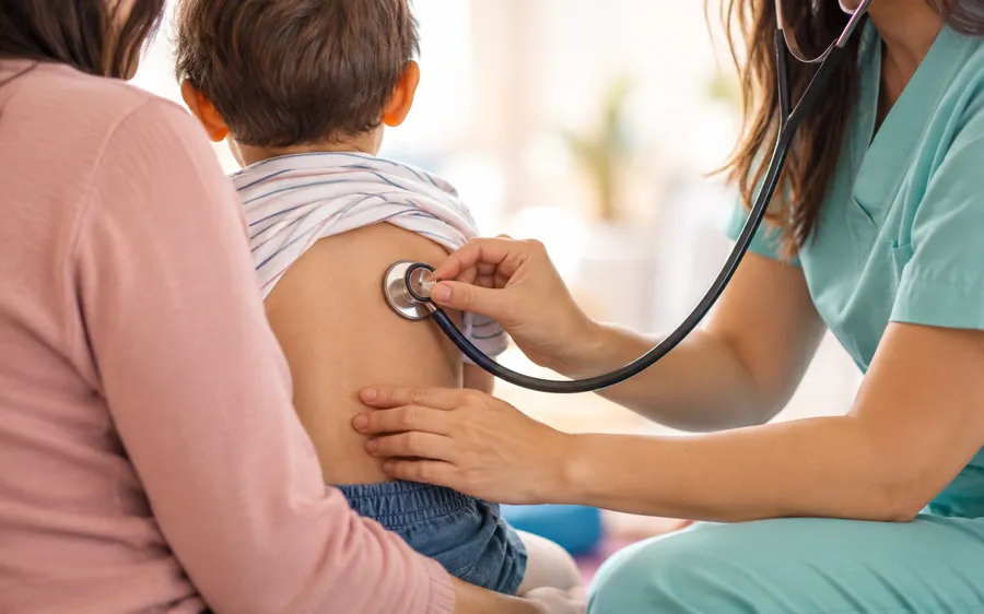 Kinesióloga auscultando la espalda de un niño en brazos de su madre